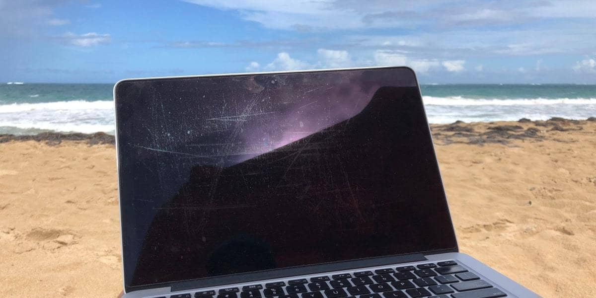 laptop screen on a beach, with sand and waves behind it.